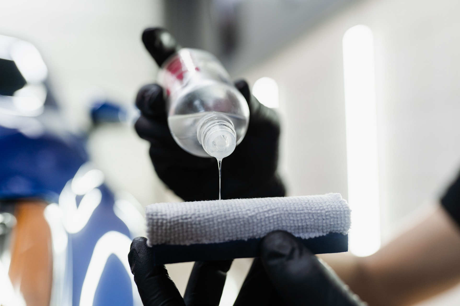 Detailing service worker applies ceramic protective liquid on sponge close-up. Process of pouring ceramic liquid from bottle on sponge to apply protective coating on car.